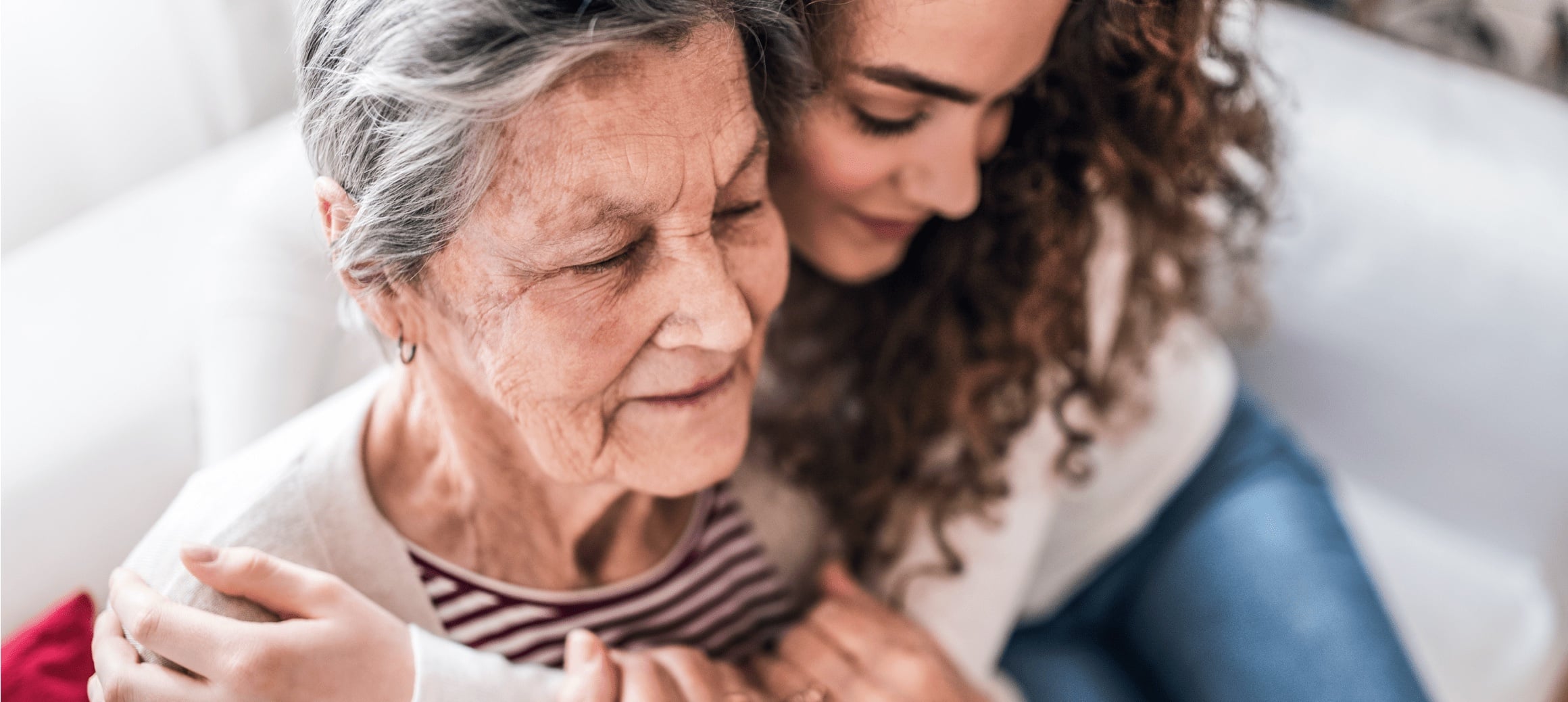 younger woman wrapping her arms around an older woman, both smiling